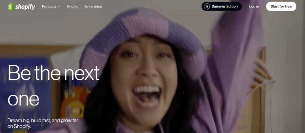 Persona joven sonriente con gorro lila y brazos levantados celebrando frente a la pantalla principal del sitio web de Shopify, donde se lee el mensaje “Be the next one”.